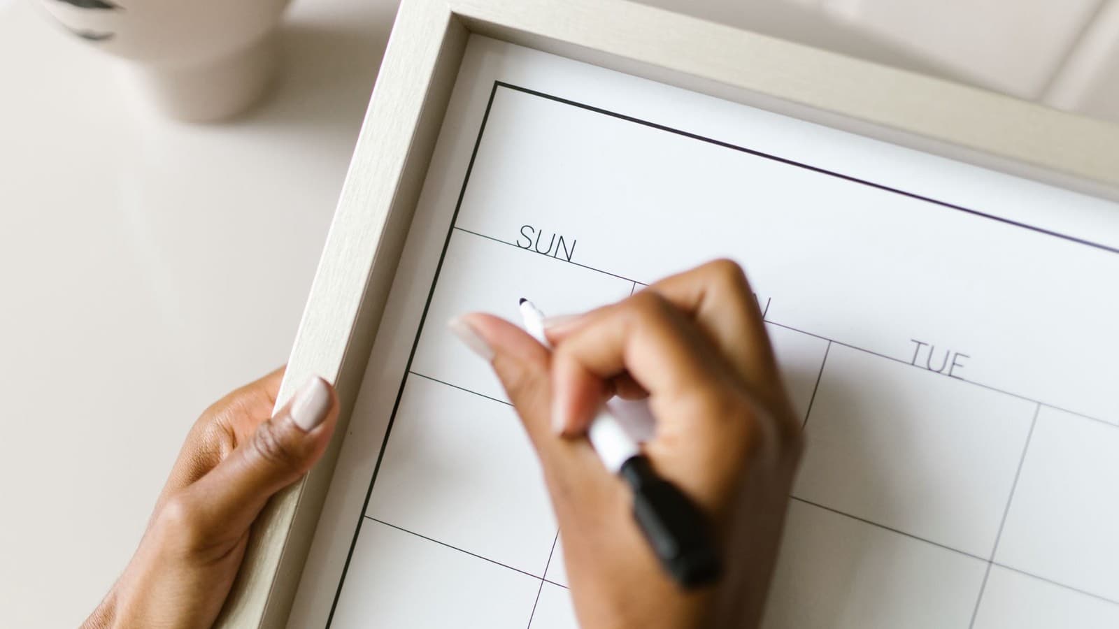 Hands holding a framed wall calendar and writing on it with a marker.